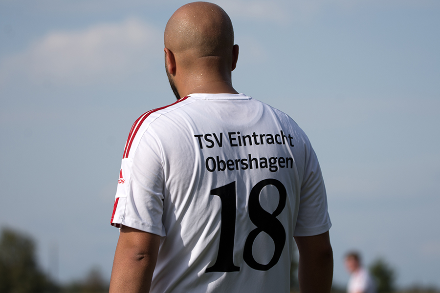Ein Fußballspieler in einem weißen Trikot mit der Nummer 18 und dem Vereinsnamen "TSV Eintracht Obershagen" auf dem Rücken steht mit dem Rücken zur Kamera.