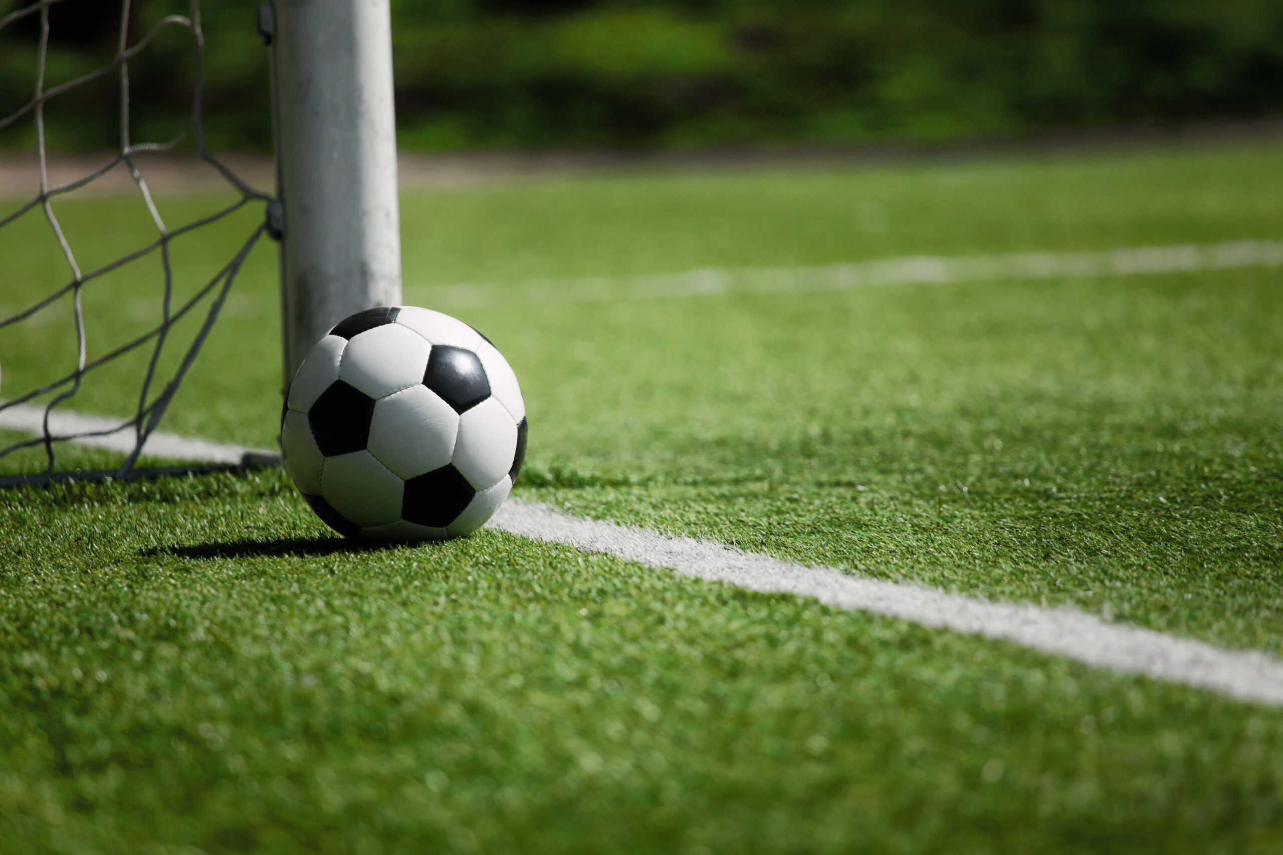 Ein Fußball liegt an einem Torpfosten auf einem Fußballfeld.